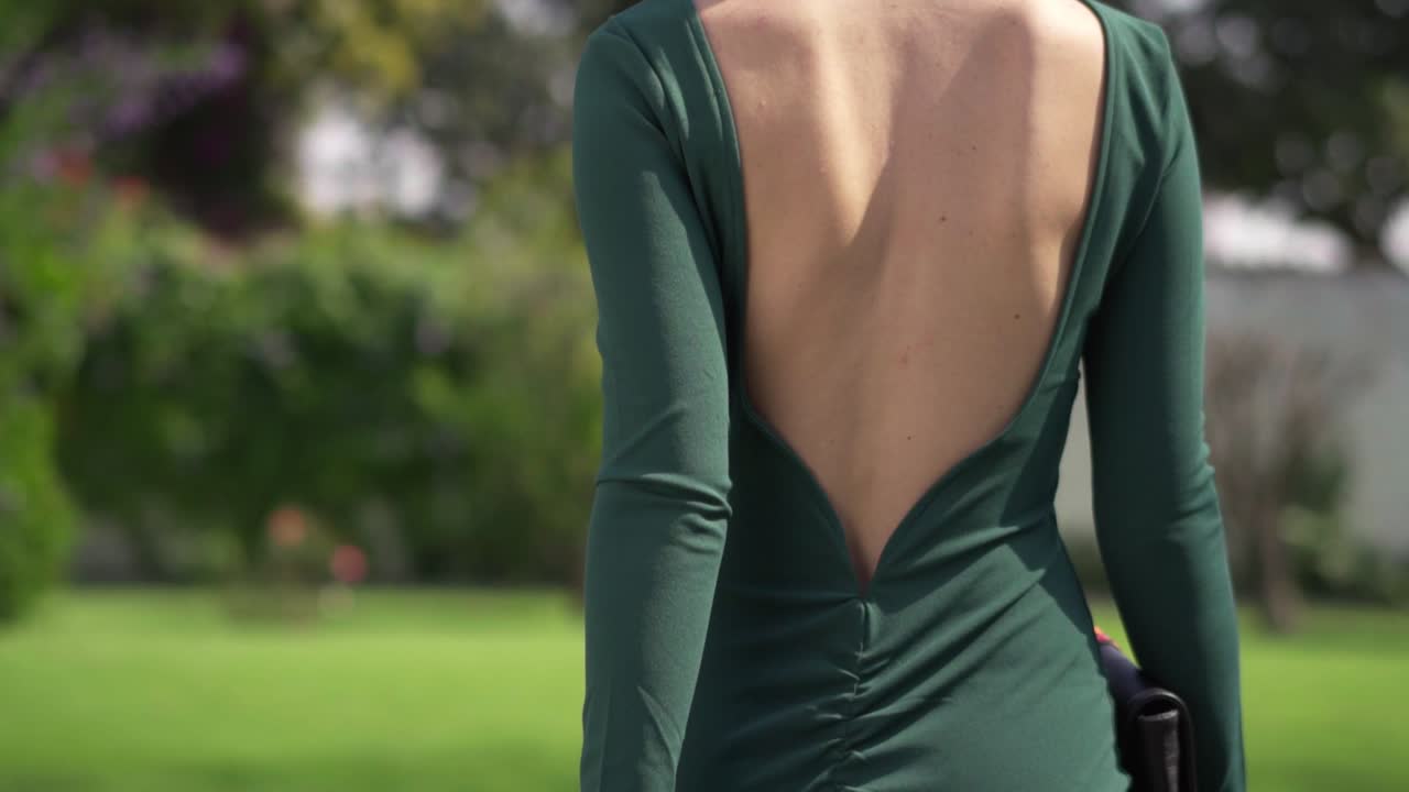 Beautiful woman turns and walks in sunny day wearing green dress