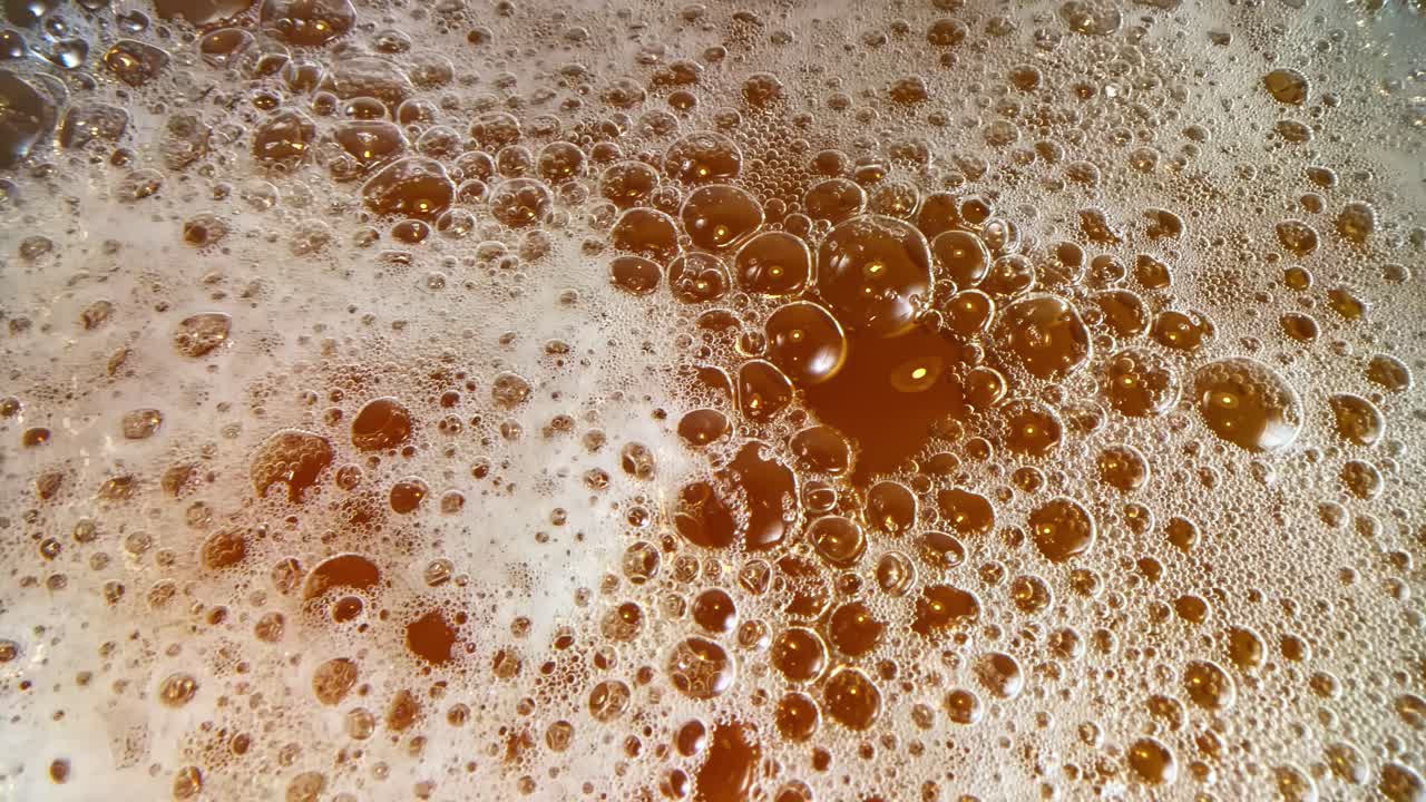 Beer alcoholic beverage up-close bubbles foam, amber dark brown homemade drink