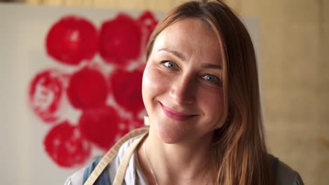 portrait shot of the beautiful and open caucasian long haired woman artist looking to the camera at her cozy art studio and smiling cheerfully