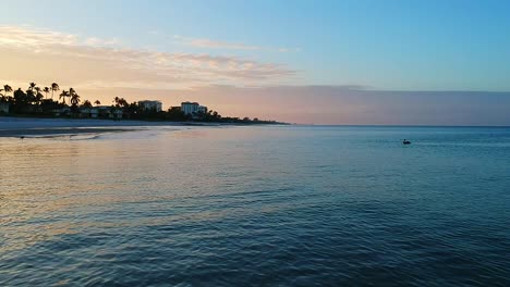 Flying-above-the-waves-at-the-beach-looking-at-the-beautiful-sunrise-with-pelicans-swimming-in-the-distance