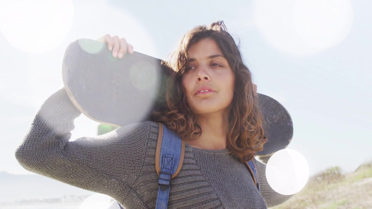 Luce solare che crea un bagliore crescente, donna con skateboard che sposta lo sguardo e aggiusta la presa mentre cammina verso le dune