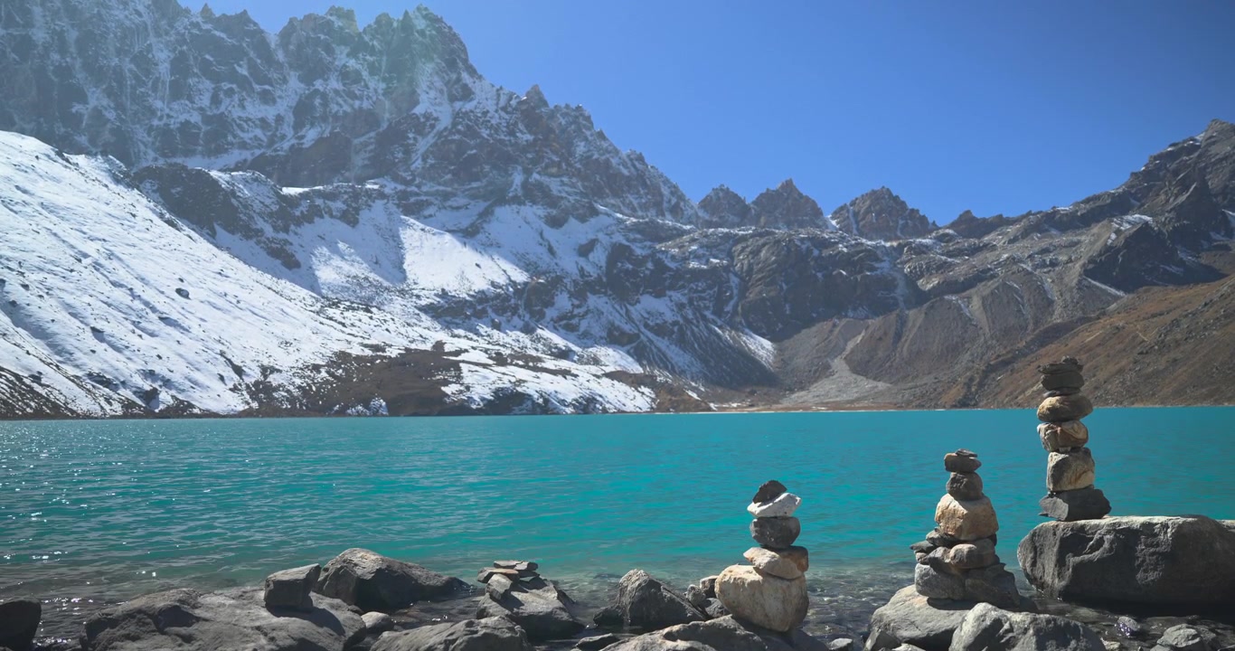 Lago Gokyo, Everest, Nepal, ampia inquadratura statica di tradizionali ometti di pietra impilati lungo la riva rocciosa di un lago alpino turchese brillante sotto imponenti cime montuose innevate