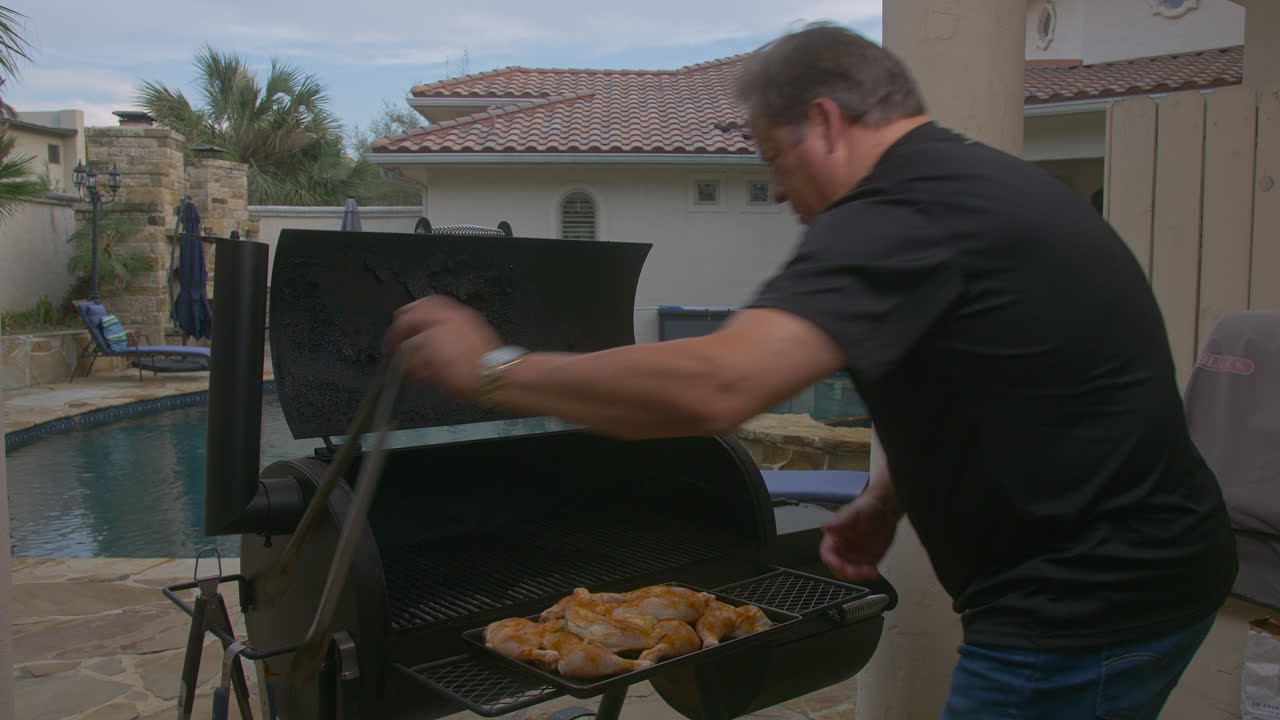 Uomo mette cosce di pollo crude sulla griglia di un barbecue fumante