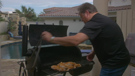 man puts raw chicken thighs on to grill in smoking bbq pit