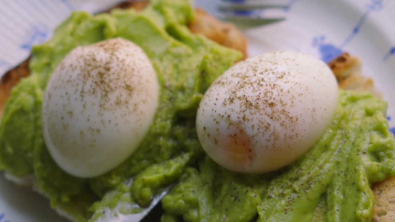 Vue de dessus d'œufs à la coque frais avec du poivre fin et de l'avocat écrasé sur du pain au levain. Petit-déjeuner sain et faible en gras.