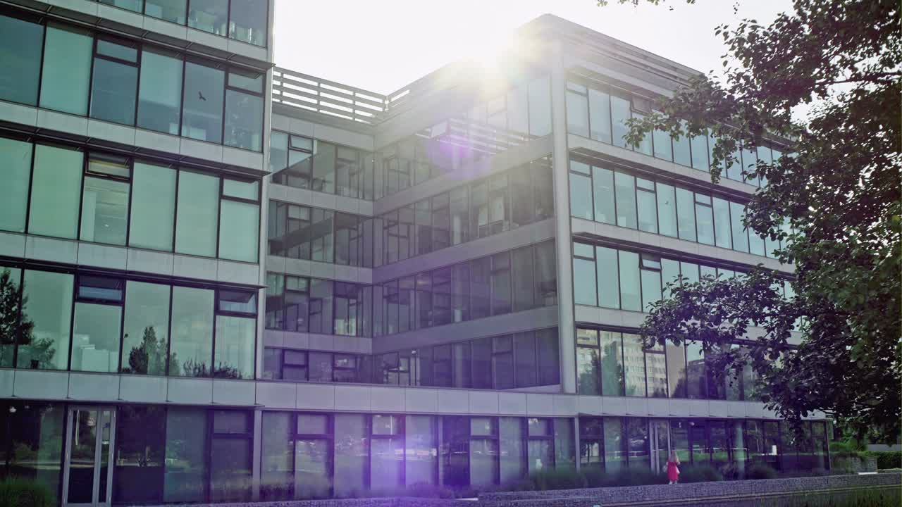 Slow pan across a modern glass office block facade with bright sun flare over the roof