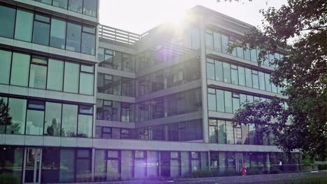 slow pan across a modern glass office block facade with bright sun flare over the roof