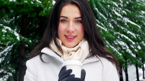 mujer sonriente con ropa cálida tomando café durante la nevada