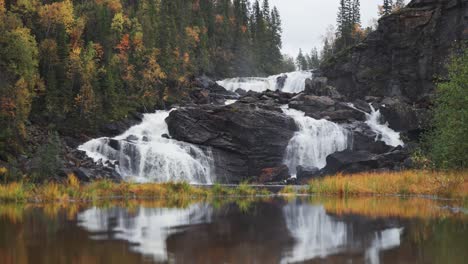 Ein-Wasserfall-Stürzt-über-Dunkle-Klippen,-Seine-Schönheit-Spiegelt-Sich-Auf-Der-Ruhigen-Oberfläche-Des-Darunterliegenden-Sees