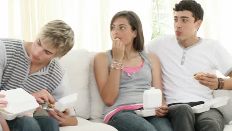 adolescentes comiendo hamburguesas y papas fritas en el sofá