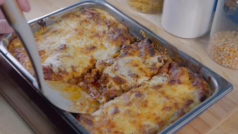 medium shot of serving a portion of lasagne from the baking tray on the kitchen counter