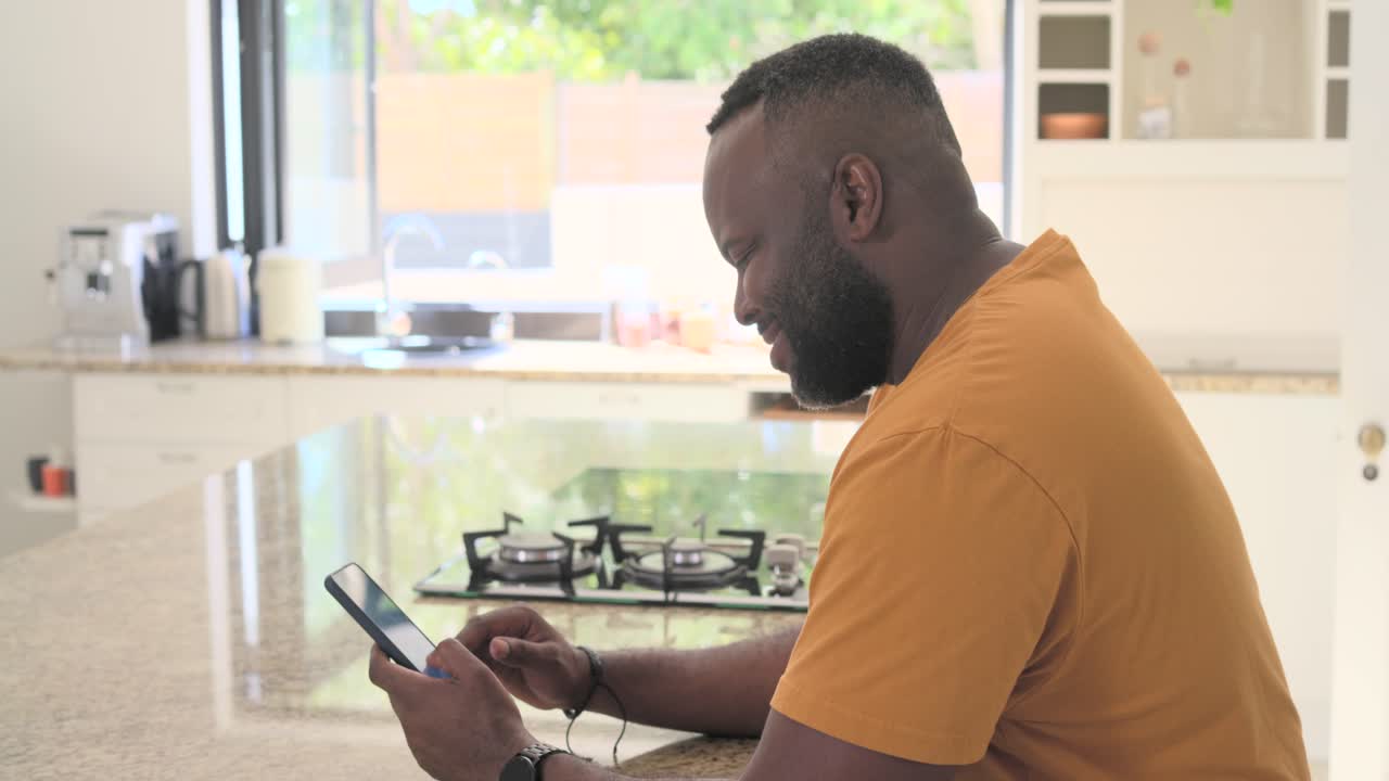 Adult African man reacting to content, holding tablet tapping screen at kitchen island, copy space