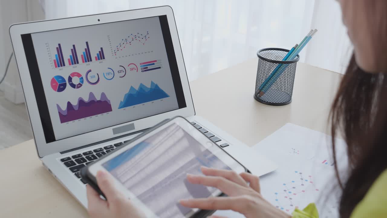 joven mujer de negocios asiática trabajando en una computadora portátil y buscando gráfico y gráfico de informe para obtener ganancias en una tableta en la oficina de casa, mujer de negocios buscando inversión e ingresos, datos de infografía.