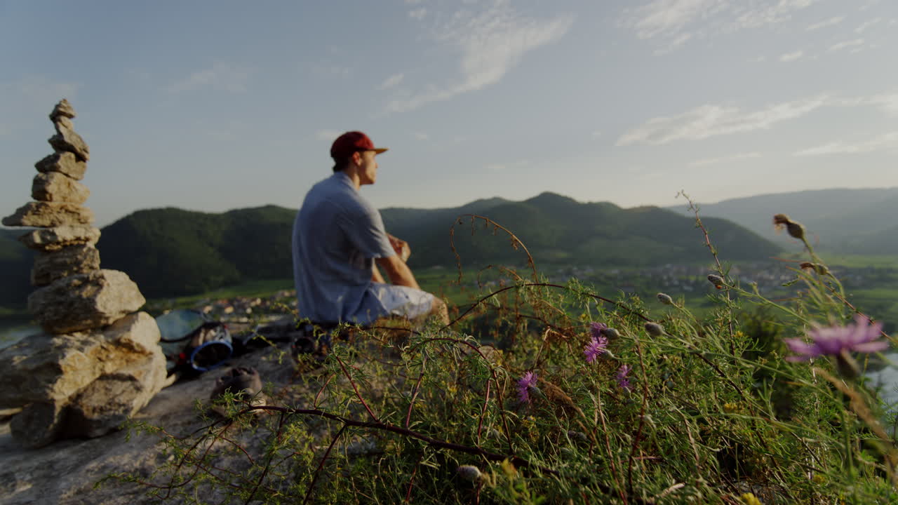 평화로운 산 피크닉 장소, 꽃 ⁇ 에서 휴식을 취하는 남자, 돌 탑, 전망을 즐기고, 전망을 즐기고, 풍경 개요, 영화 속도 느린 슬로모, 남자는 야외 언덕을 즐긴다