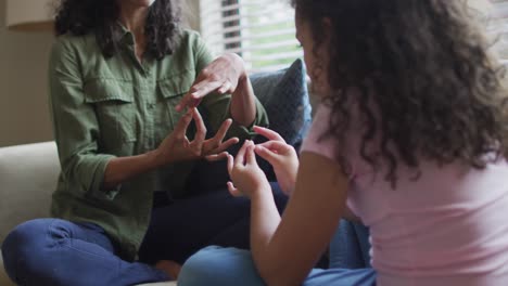 Happy-mixed-race-mother-and-daughter-playing-with-hands-in-living-room