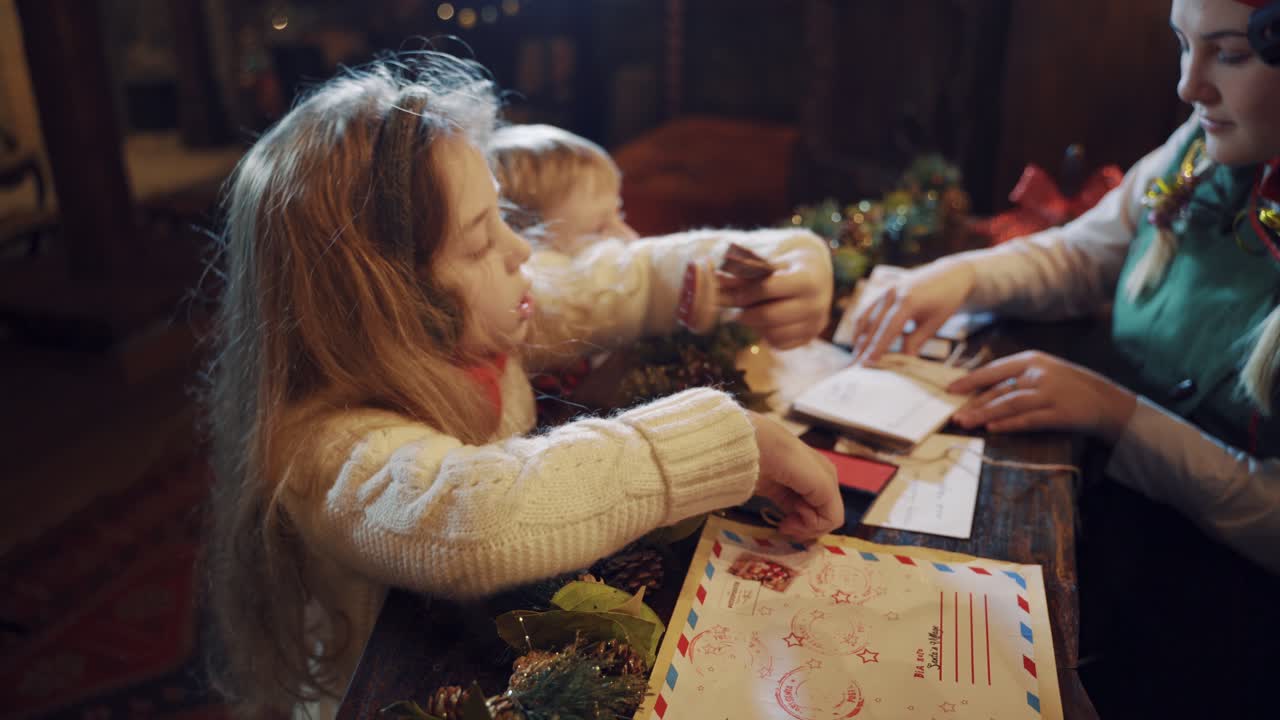 Curious girl putting signet on the envelope. Child helps elf to prepare letters at Christmas. Envelopes from Santa Claus on the table.