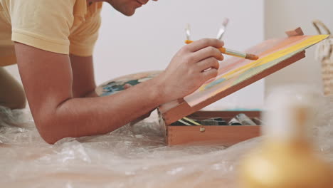 the hands of an unrecognizable man painting a canvas