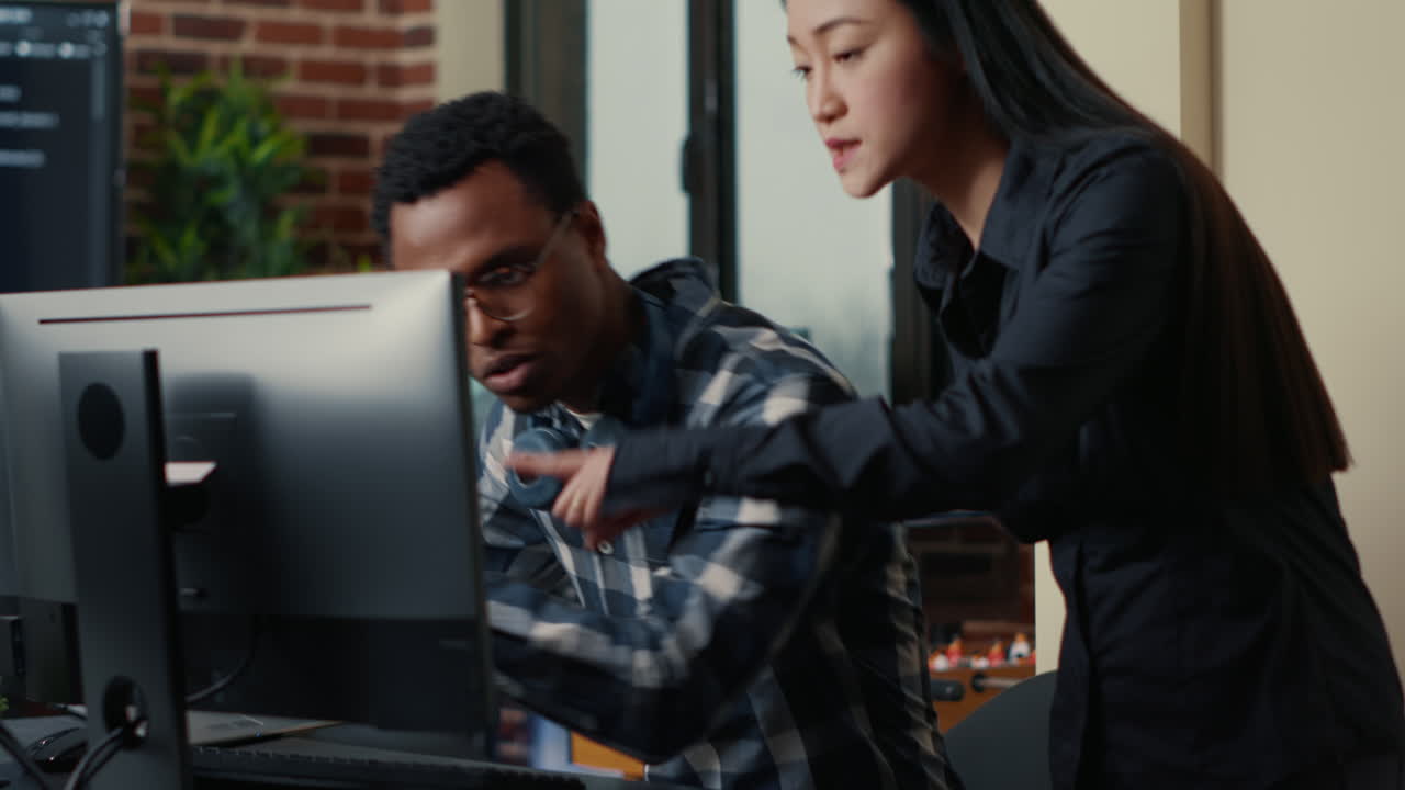 Two software developers coming at desk and sitting down holding laptop with coding interface