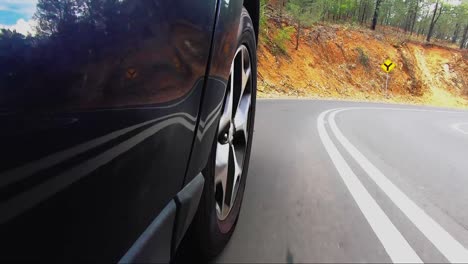 punto de vista del coche desde la carretera mirando hacia la rueda delantera derecha conduciendo por una carretera bituminosa bajando una colina hacia la ciudad