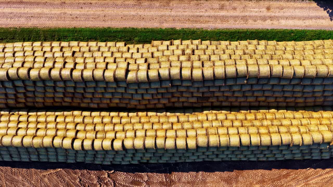 Drone pans over large stacks of hay bales arranged in tight rows on dry farmland surface