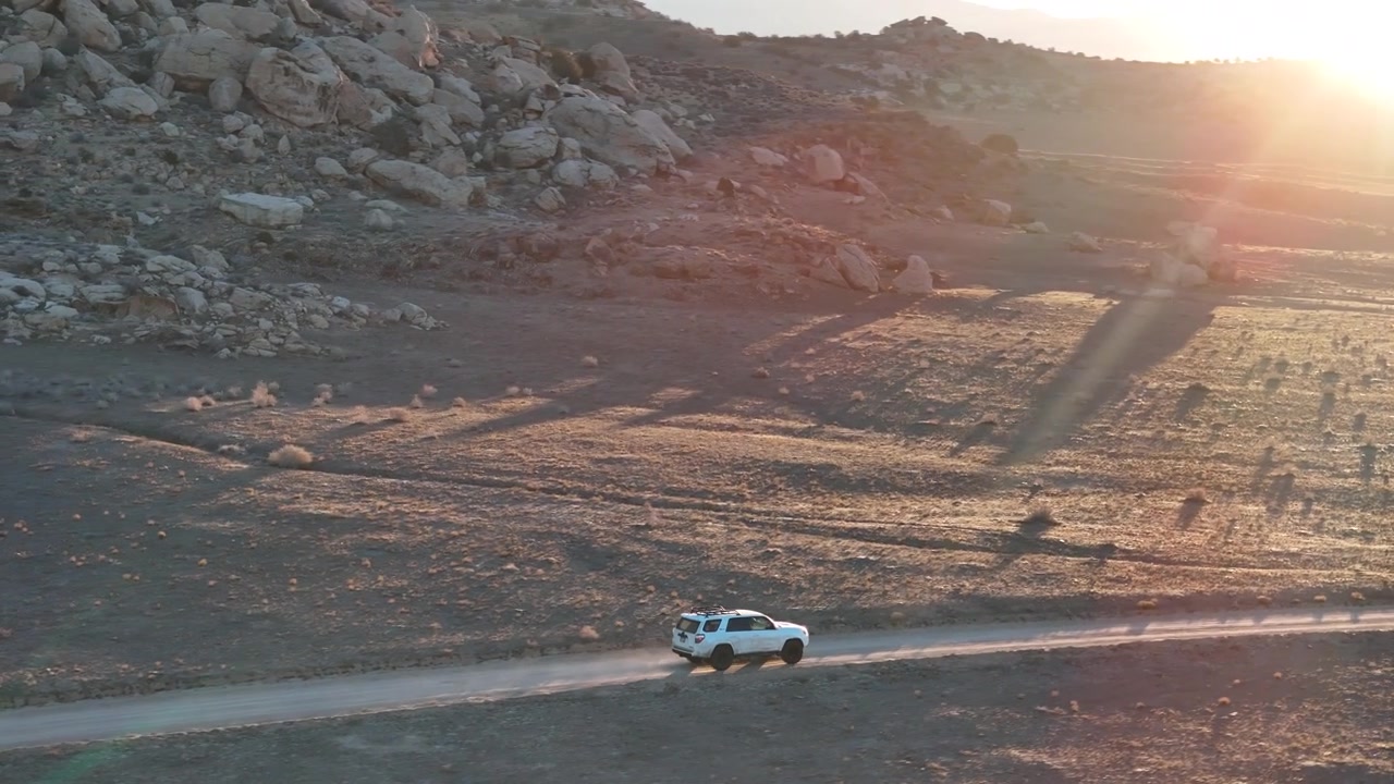 Veduta aerea di un SUV bianco su una strada nel deserto al tramonto sopra il paesaggio del confine tra Utah e Colorado, ripresa drone.