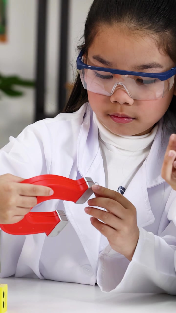 Primary school students wear safety goggles while exploring magnetism with horseshoe magnets in bright classroom.