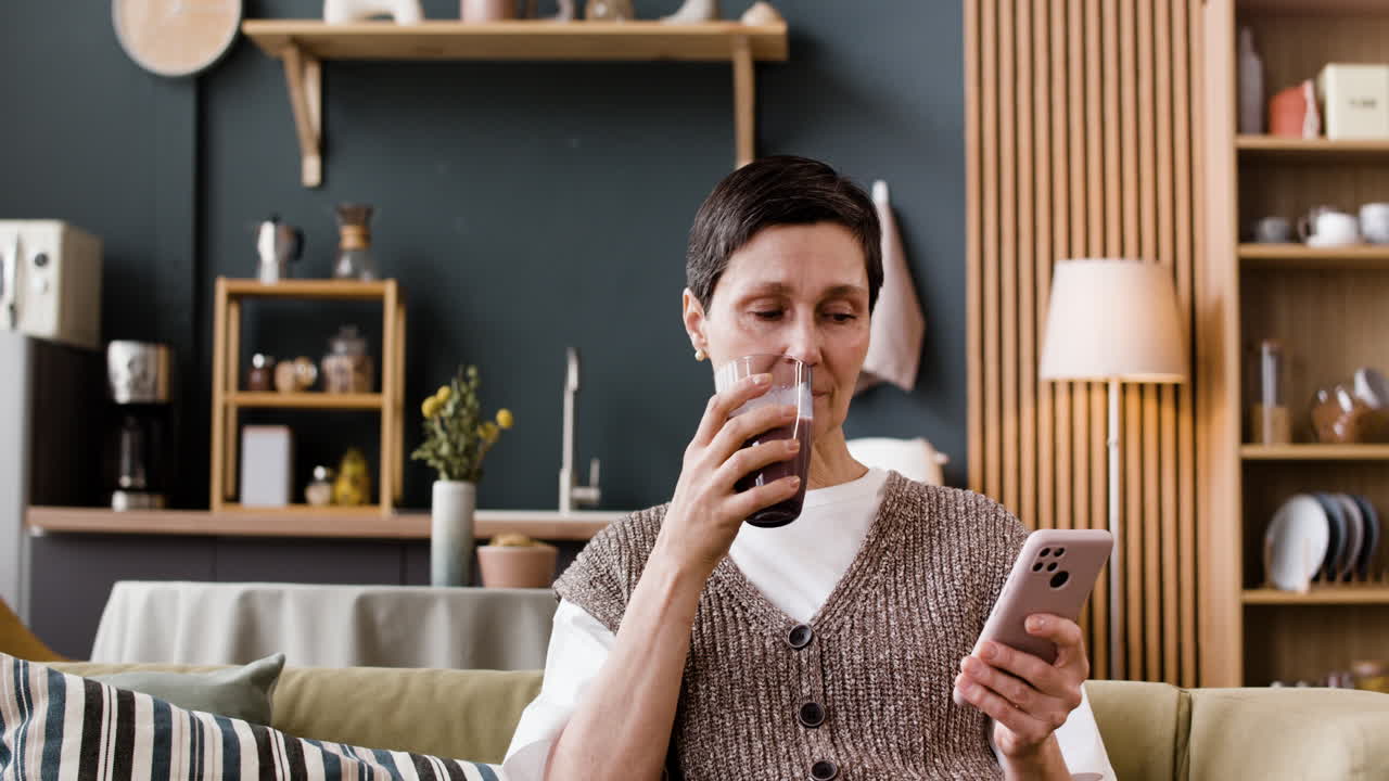 Woman on sofa drinking and using smartphone