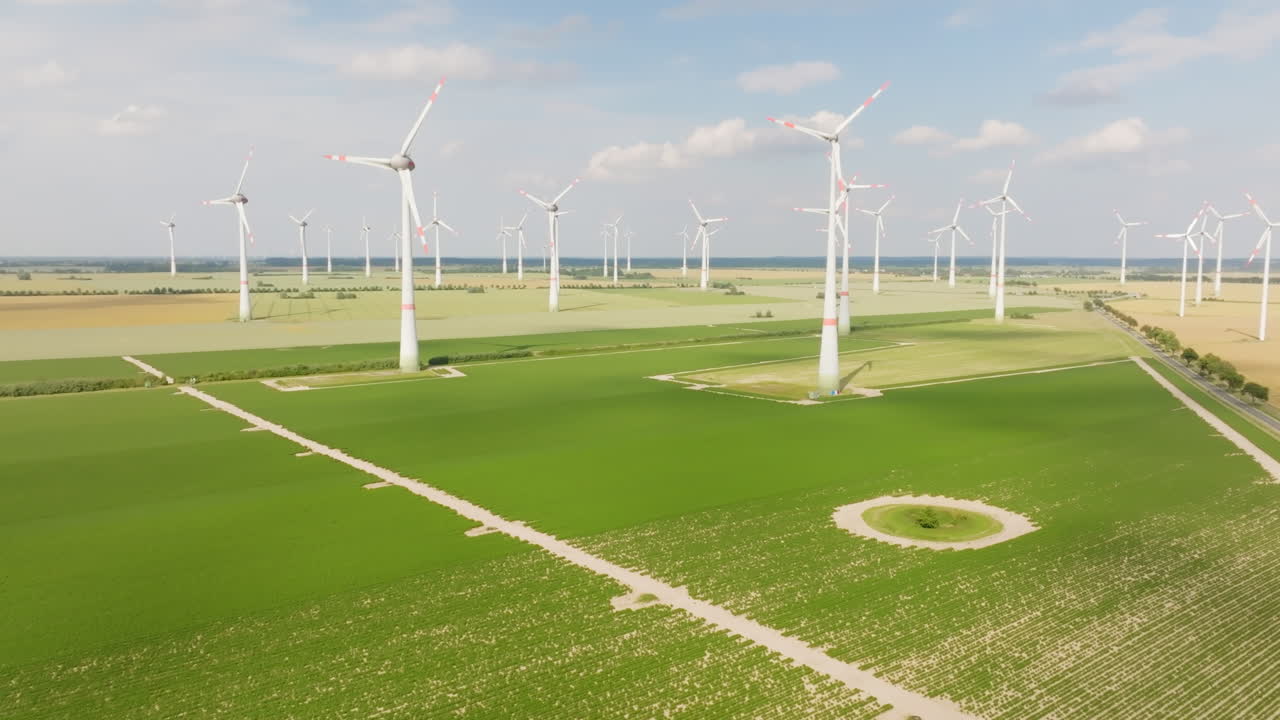 Aerial view rising over a camper van driving in front of wind turbines, sunny day