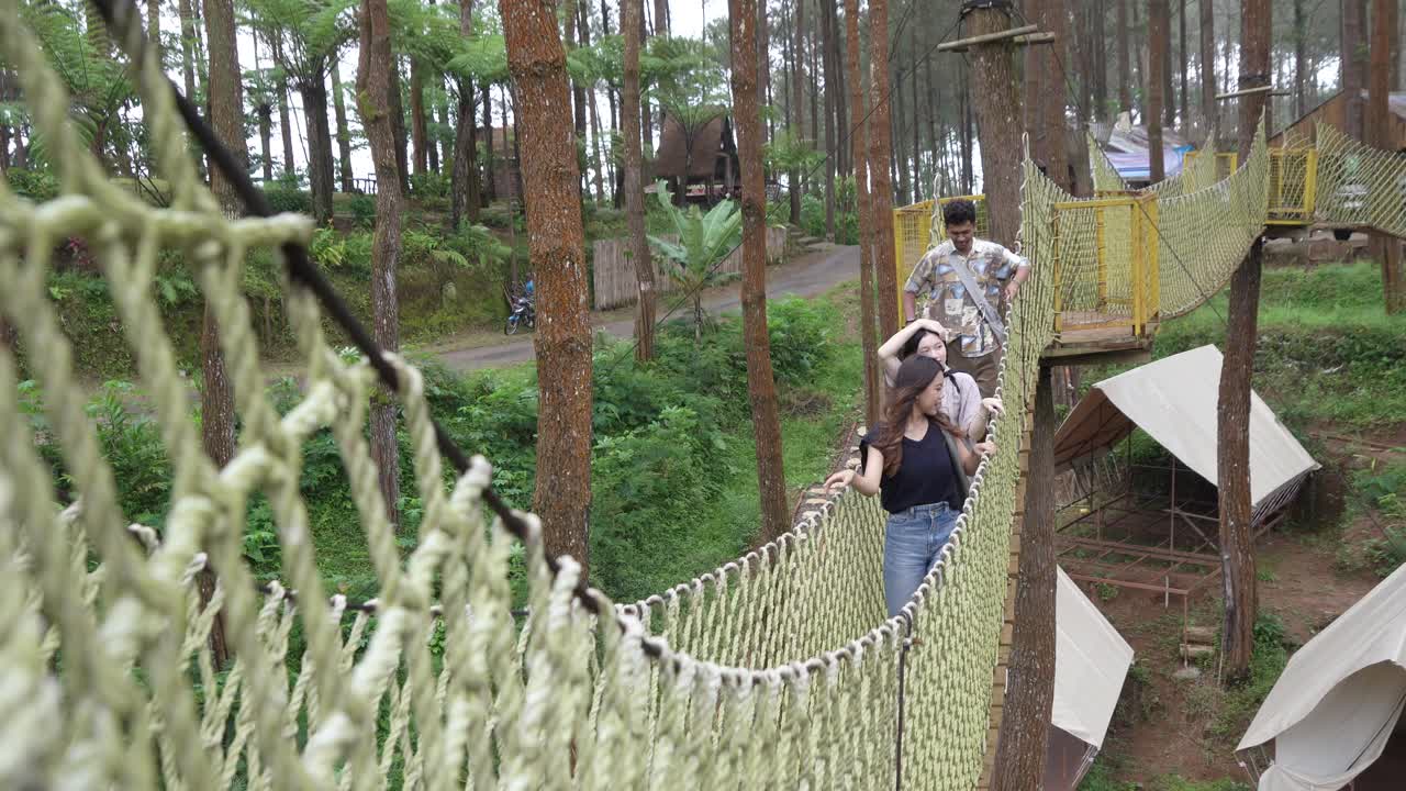 Young Asian Friends Crossing Rope Bridge in Forest Adventure