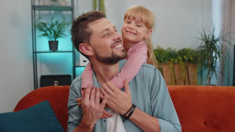 smiling child kid daughter embrace her young father, look at camera, sweet tender love at home sofa