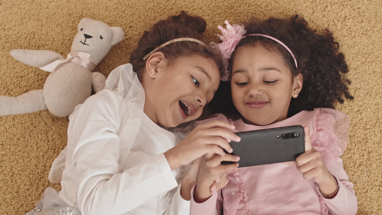 Sisters using Smartphone Lying on Floor