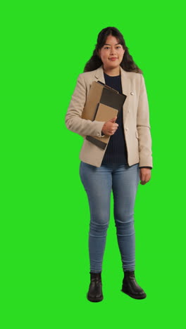 vertical video full length studio portrait of female teacher or businesswoman standing against green screen carrying folder