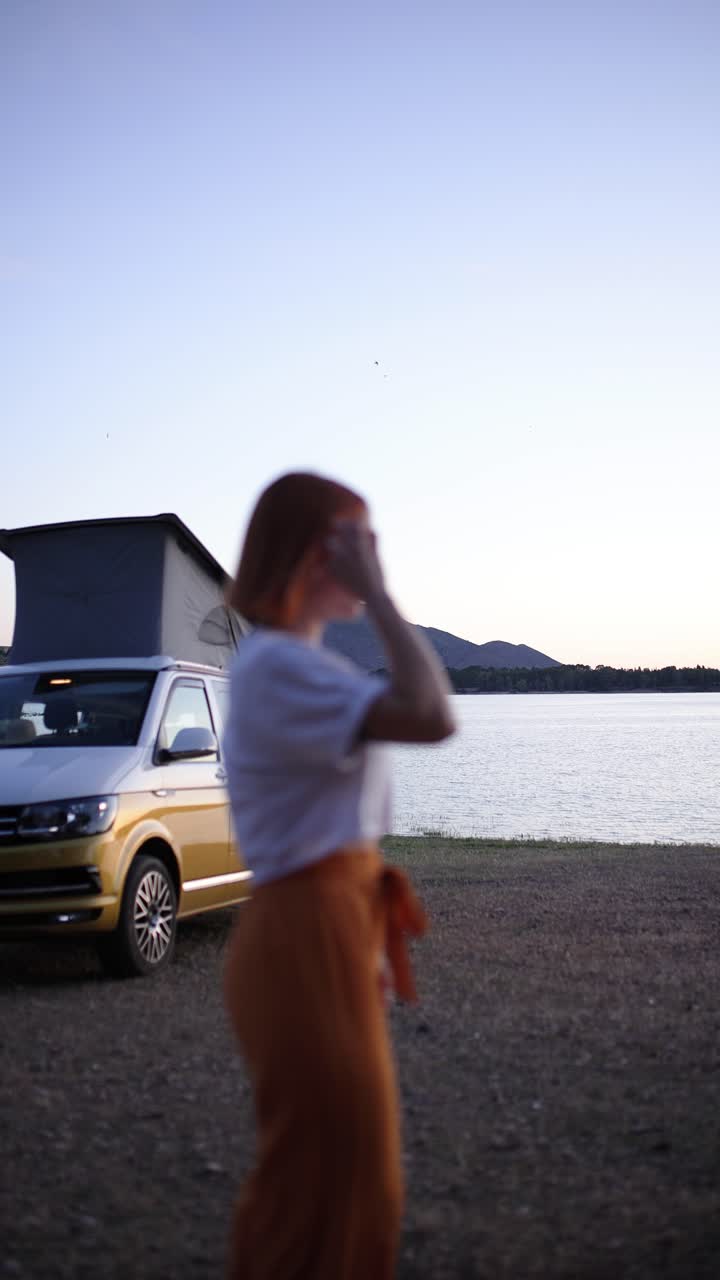 Donna in piedi accanto a un camper in riva al lago al tramonto
