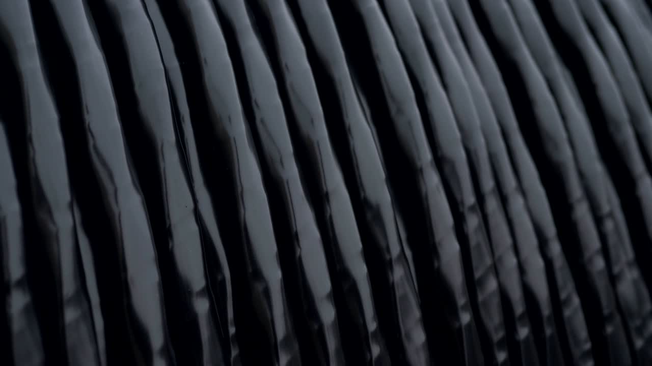 un grueso cable negro en primer plano envuelto alrededor de una enorme bobina de madera ka en la planta de cables.