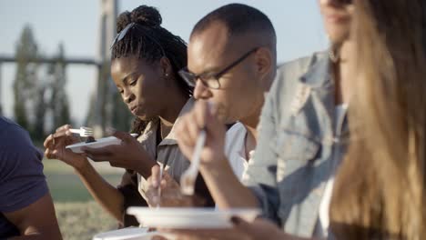 Side-view-of-smiling-friends-eating-delicious-cake-in-park