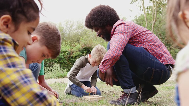 Capo squadra che mostra a un gruppo di bambini in gita in campeggio all'aperto come accendere un fuoco