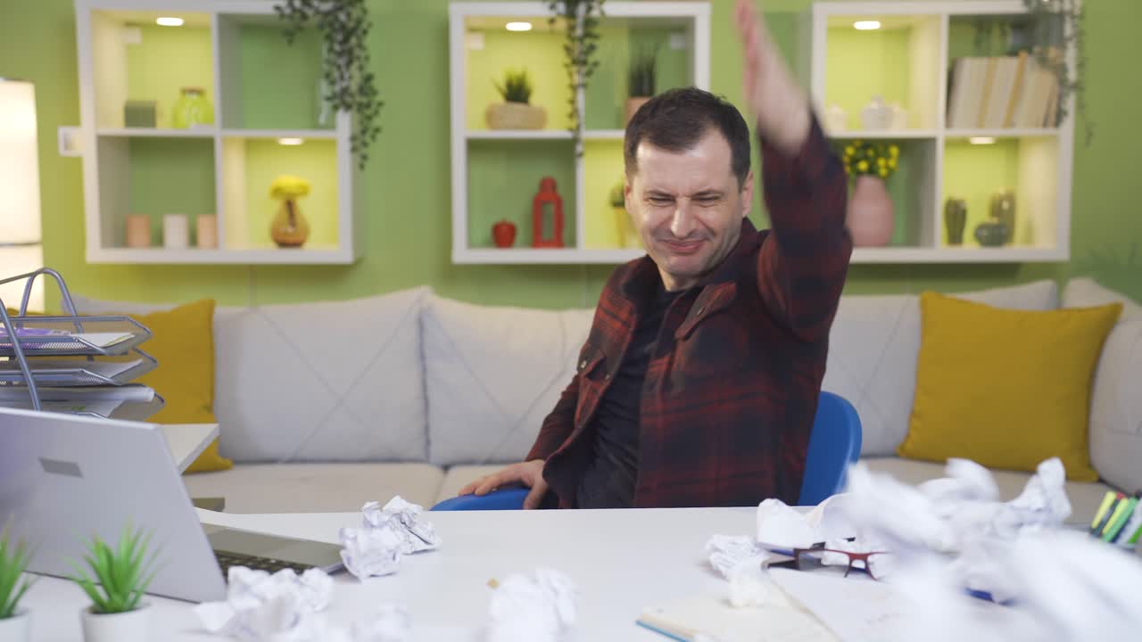 estado estresante del hombre que mira el papel en su mano y no le gusta y lo arrugas. hay un montón de papel arrugado delante de él.