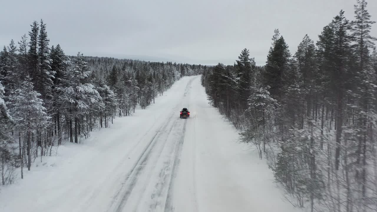 Car driving on a road covered with snow and ice through the countryside of Finland. Aerial follow shot