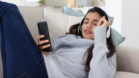 Relaxing on sofa, woman listening to music with headphones and smartphone