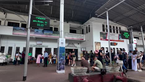 kandy train station with travelers and digital information boards displaying schedules. the platform is crowded with people waiting for their trains in sri lanka.