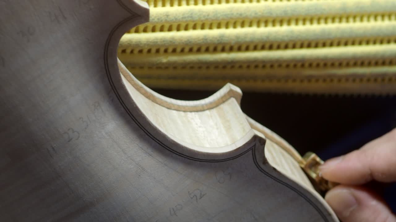 Close-up of artisan shaping the violin’s top plate edge near the f-hole with a small brass gouge, refining the edgework and purfling channel for precise curvature and smooth transitions before varnish