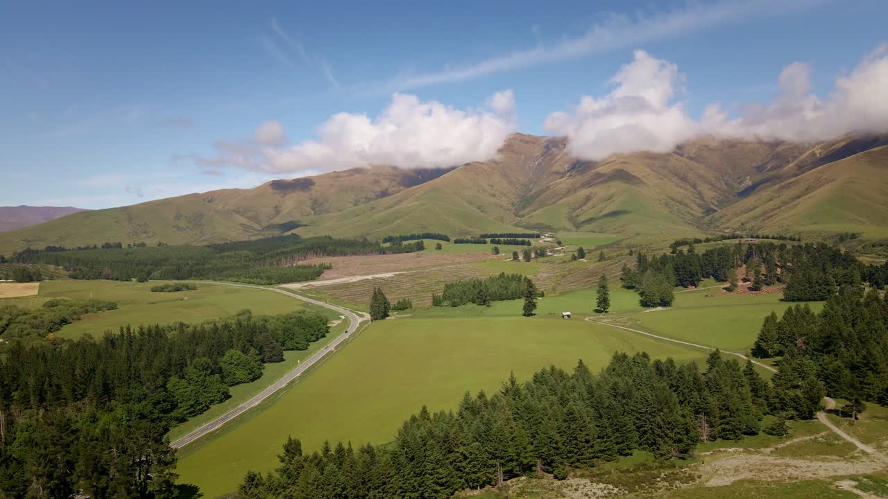 Aerea - Terreni agricoli e foreste di fronte a belle montagne con alcune nuvole basse in una mattinata di sole.