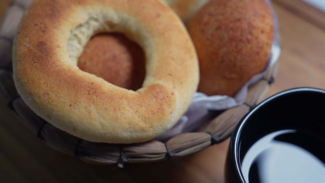 A close-up shot of Colombian pandebono bread, golden and fresh in a woven basket. Rich texture and warm lighting create a cozy, inviting atmosphere perfect for culinary themes