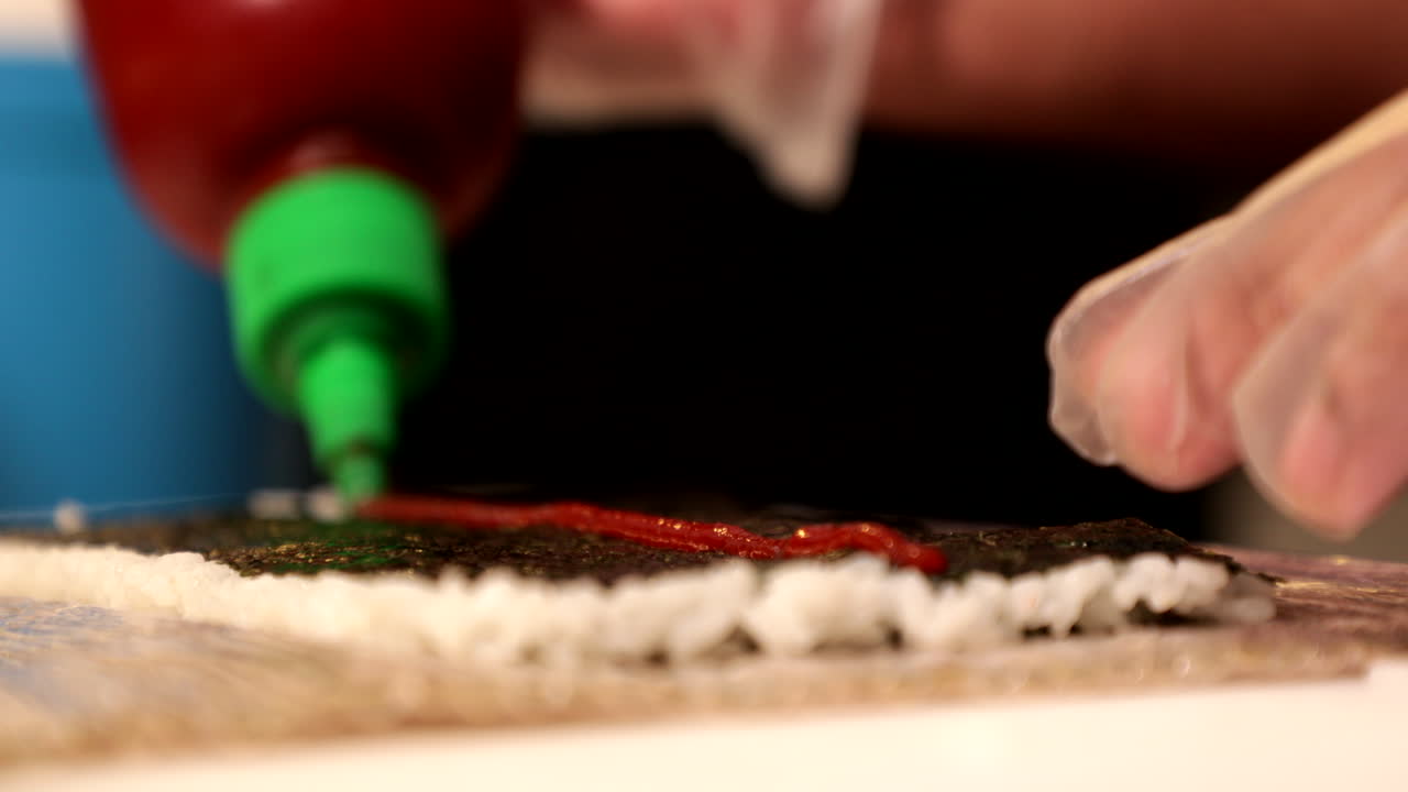 añadiendo salsa roja al nori con arroz de sushi - enfoque selectivo, primer plano