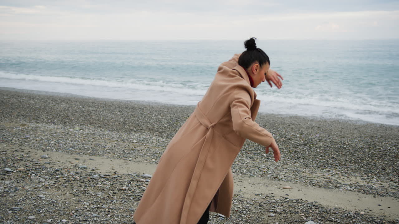 On The Dull Ocean Shore A Woman In Brown Coat Dances To Slow Rhythm Music