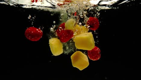 Super-slow-motion-of-fresh-mango-and-pineapple-falling-into-water-on-black-background