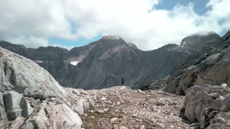 Drone-shoot-near-the-ground,-with-a-Hiker-standing-on-the-edge-of-a-remote-valley-with-a-big-granite-wall-on-the-background