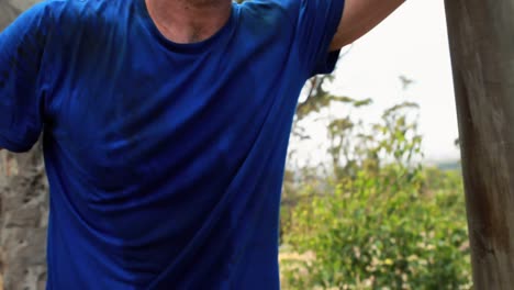 Portrait-of-fit-man-leaning-on-wooden-pole-during-obstacle-course