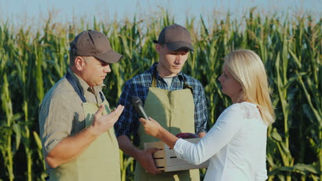 a reporter with a microphone records interviews with two farmers stand in the field against the back