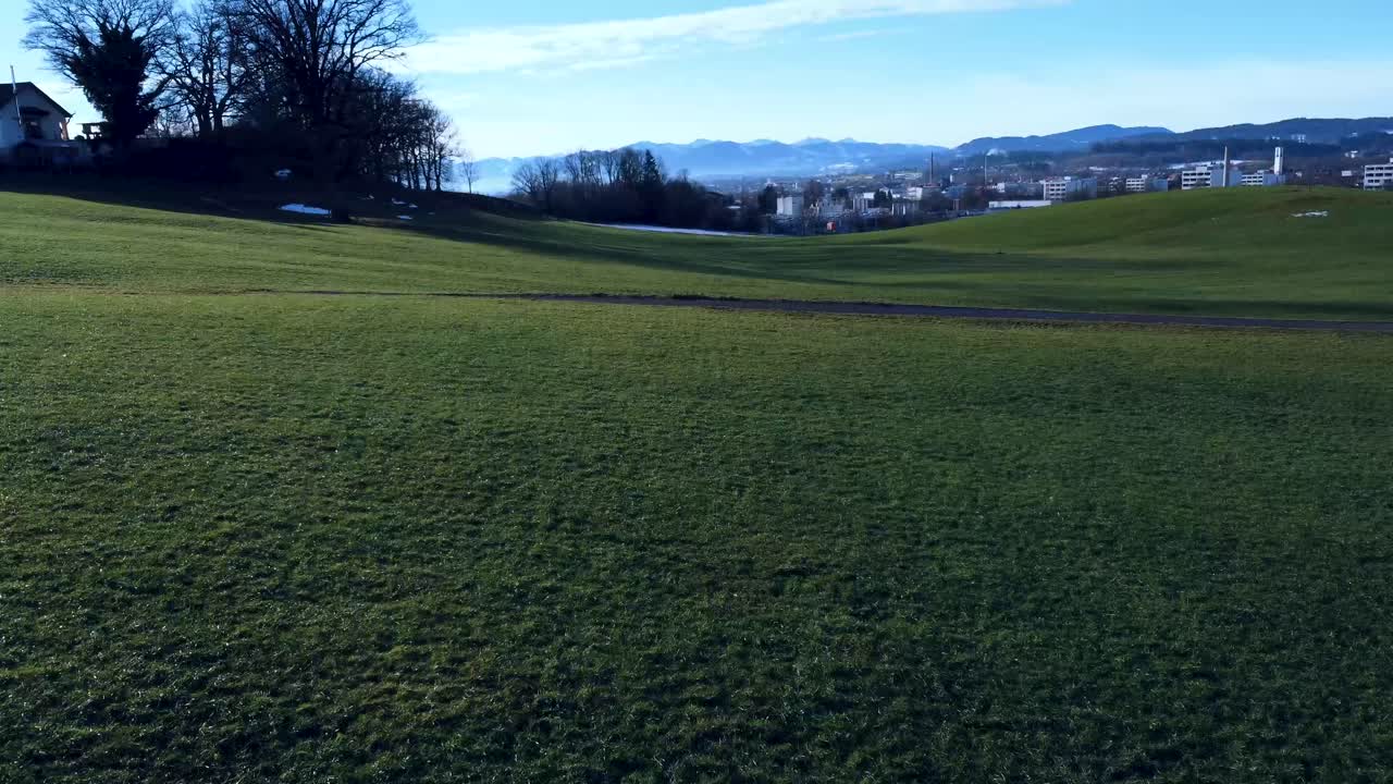 드론이 지면 근처에서 윙윙거리고, 멀리 알프스가 녹색 풍경 위로 날아갑니다.